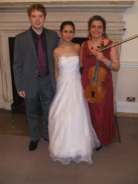 Gli sposi sorridenti con la musicista professionista dopo la ceremonia di matrimonio civile, al ricevimento nel municipio di Woodstock, vicino a Oxford. La tua musica preferita suonata sulla viola